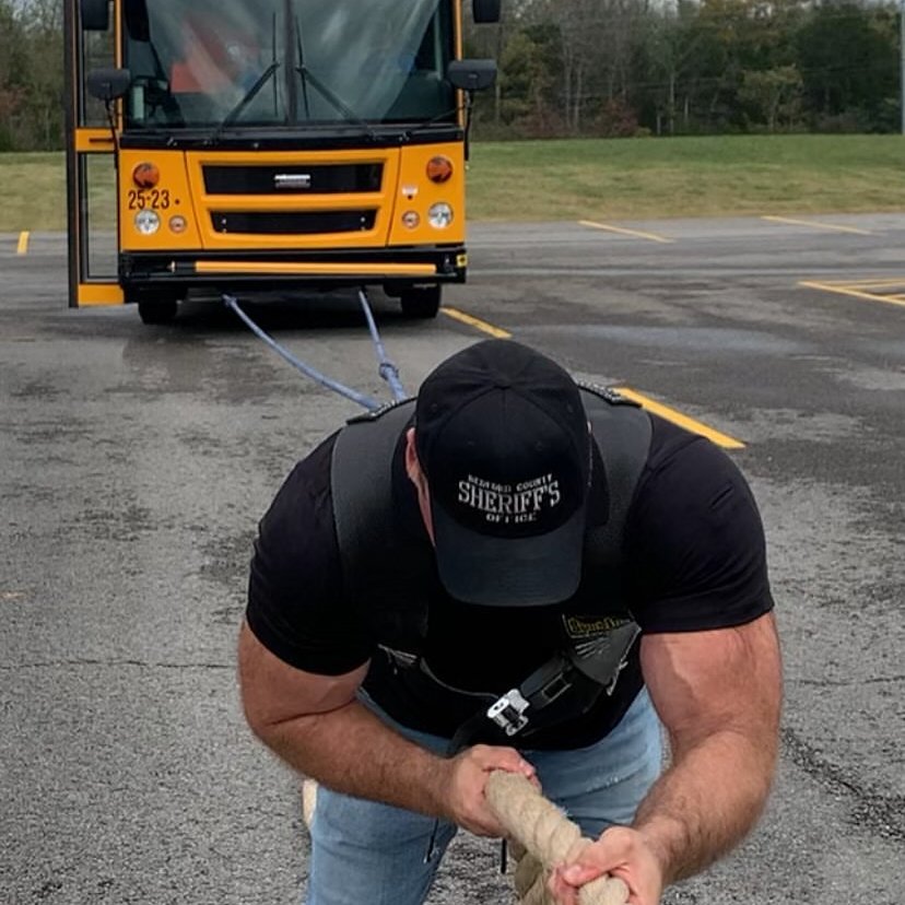Tim, a strong man, is pulling a large bus using his strength.